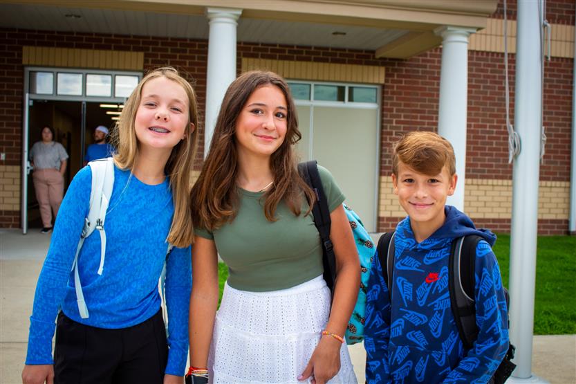 Students smile in front of school on the first day